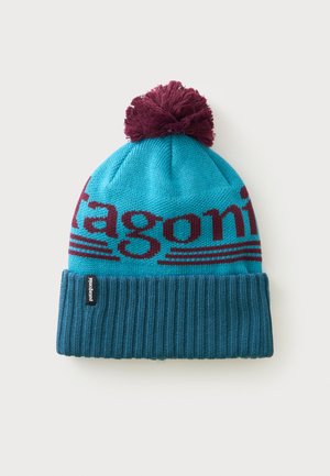 Bonnet tricoté bleu avec pompon rouge foncé et revers côtelé, avec texte partiel rouge foncé "Patagonia" sur la partie principale.