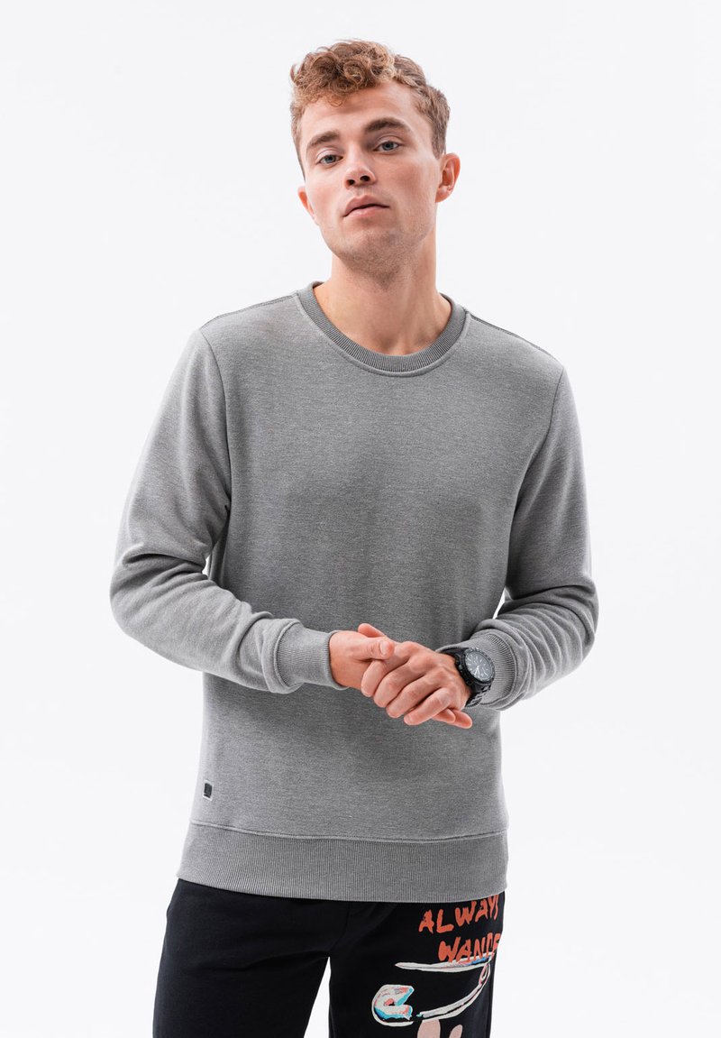 Grå sweatshirt med lange ærmer, rund halsudskæring, ribbede manchetter og kant. Bæres over sorte bukser med farverig tekst og designs.