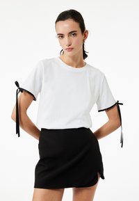 Witte katoenen t-shirt met korte mouwen, voorzien van zwarte lintaccenten op de mouwen, gecombineerd met een zwarte strakke mini-jurk.
