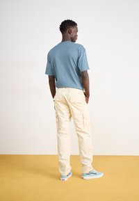 Light blue short-sleeve t-shirt, cream cargo pants, and blue sneakers. The t-shirt is soft, while the cargo pants have multiple pockets.
