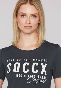Camiseta de color azul marino oscuro con texto blanco en negrita que dice "VIVE EL MOMENTO SOCcx MARCA REGISTRADA Original". Diseño clásico de cuello redondo.