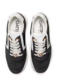 Schwarz-weiße Sneakers mit einer strukturierten Oberseite, Schnürverschluss, goldenen Hardware-Akzenten und einer gepolsterten Sohle. Markenname sichtbar im Inneren.