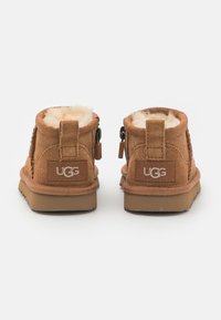 Braune Wildleder-Ankle-Boots mit Schaffellfutter, ausgestattet mit einem Logo-Patch und Reißverschlüssen an den Seiten. Robuste Gummisohle mit rutschfester Oberfläche.