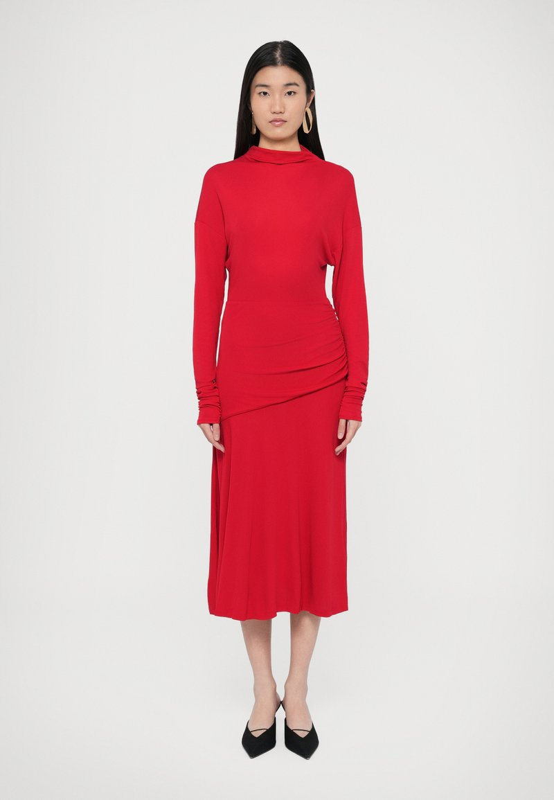 Κόκκινο φόρεμα με μακριά μανίκια, ψηλό λαιμό, εφα�ρμοστή μέση και ρυτιδωμένη λεπτομέρεια στο πλάι. Λείο, ελαστικό ύφασμα με ροή σε μέτριο μήκος.