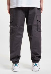 Cargo bukser i mørkegrå stof, med elastiske manchetter og side lommer. Båret med hvide sneakers, der har turkise accenter.