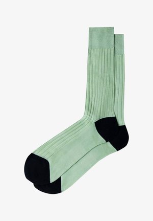 Par de calcetines de color verde claro con diseño acanalado y secciones sólidas negras en el talón y la punta, mostrados uno al lado del otro sobre un fondo blanco.