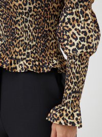 Blouse à imprimé léopard avec corsage smocké et manches bouffantes. Le tissu présente des taches noires et marron sur un fond beige. Manches à volants.