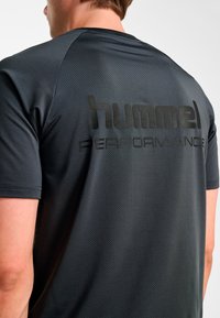 Czarna sportowa koszulka z teksturowanym wzorem, z wyraźnym czarnym logo "hummel PERFORMANCE" na plecach. Krótkie rękawy, okrągły dekolt.