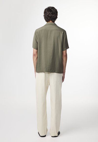 Camicetta corta verde oliva a maniche corte con una finitura testurizzata, abbinata a pantaloni larghi a pieghe color crema.