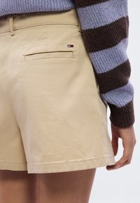 Μπεζ βαμβακερά σορτς με πίσω τσέπη, που διαθέτουν ένα μικρό λογότυπο σε κόκκινο, λευκό και μπλε. Το ύφασμα έχει λεία υφή και καθαρό ράψιμο.