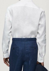 Witte linnen blouse met lange mouwen en knoopmanchetten, gecombineerd met donkerblauwe op maat gemaakte broek met achterzakken en een lichte textuur.