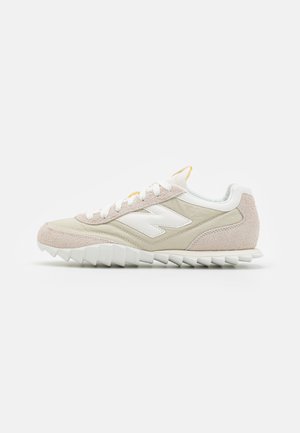 Basket avec une tige en suède beige et synthétique crème, des lacets blancs et une semelle blanche texturée avec des crampons de traction proéminents.