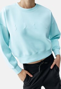 Kort sweatshirt in lichtblauw, met verhoogd BDR-logo detail, geribbelde halslijn en een losse fit. Gekocht met zwarte joggingbroek met trekkoord.