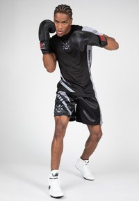 Zwarte boksshort en een bijpassend shirt met korte mouwen, accentueert met grijze details. Het model draagt zwarte bokshandschoenen en witte schoenen.