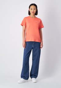 Koraalrood katoenen T-shirt met korte mouwen en een ronde hals, gecombineerd met blauwe wijdvallende denim jeans en witte sneakers.