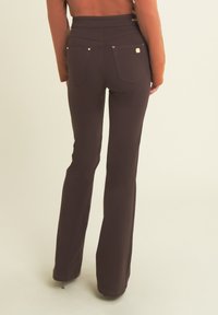 Pantalones acampanados marrones con una textura suave, que presentan una cintura alta, bolsillos traseros y costuras decorativas. Se aprecian acentos de hardware metálico.