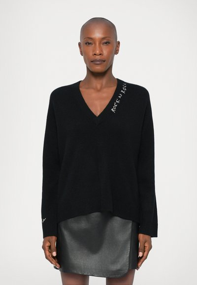 Black V-neck sweater with long sleeves, featuring white "Rock 'N' Roll" embroidery on the shoulder. Paired with a black leather skirt.