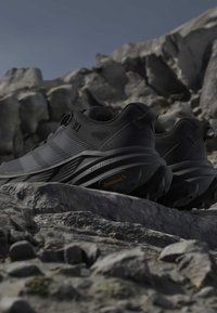 Chaussures de trail noires avec semelles robustes Continental posées sur un terrain rocheux sous un ciel dégagé.