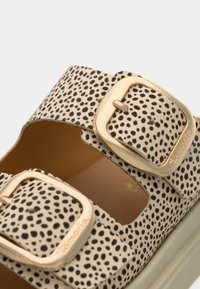 Sandale en cuir beige avec des pois noirs, deux brides réglables avec boucles en or et une semelle intérieure texturée.