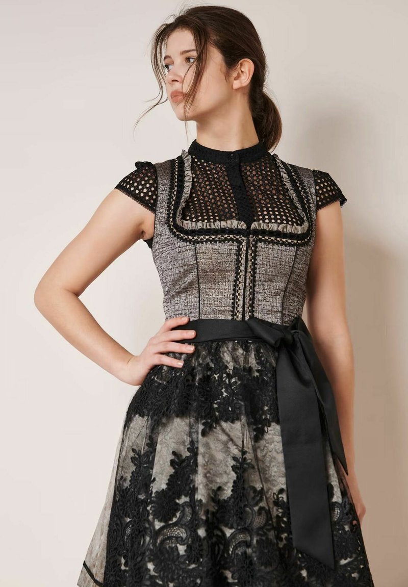 Schwarz-graues Kleid mit einem strukturierten Oberteil und einer Spitzenbedeckung sowie einer taillierten Taille. Akzentuiert mit einem schwarzen Band und aufwändigen Spitzen_details.