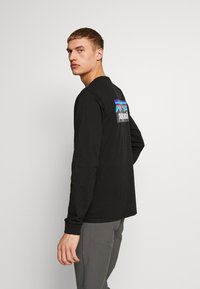 Sort langærmet T-shirt med et farverigt bjerggrafik og logo på ryggen. Stof ser glat ud med en afslappet pasform.