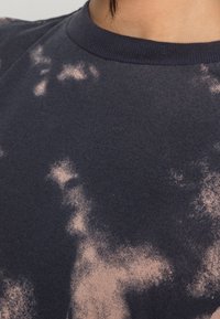 Maglietta in cotone blu navy con un sottile motivo tie-dye rosa, caratterizzata da un collo rotondo e una consistenza morbida. Accenti di colore chiaro in tutto il capo.