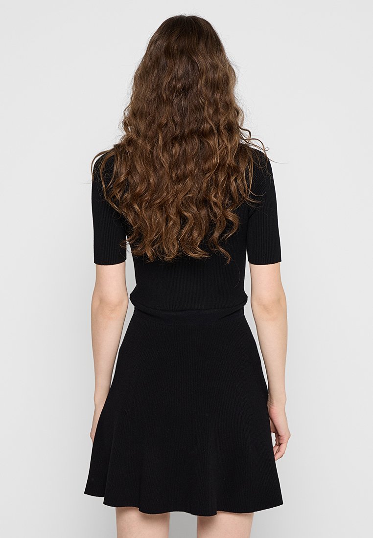 Robe noire côtelée avec un haut ajusté et une jupe évasée. Manches courtes avec une texture lisse et un design sans coutures à la taille.