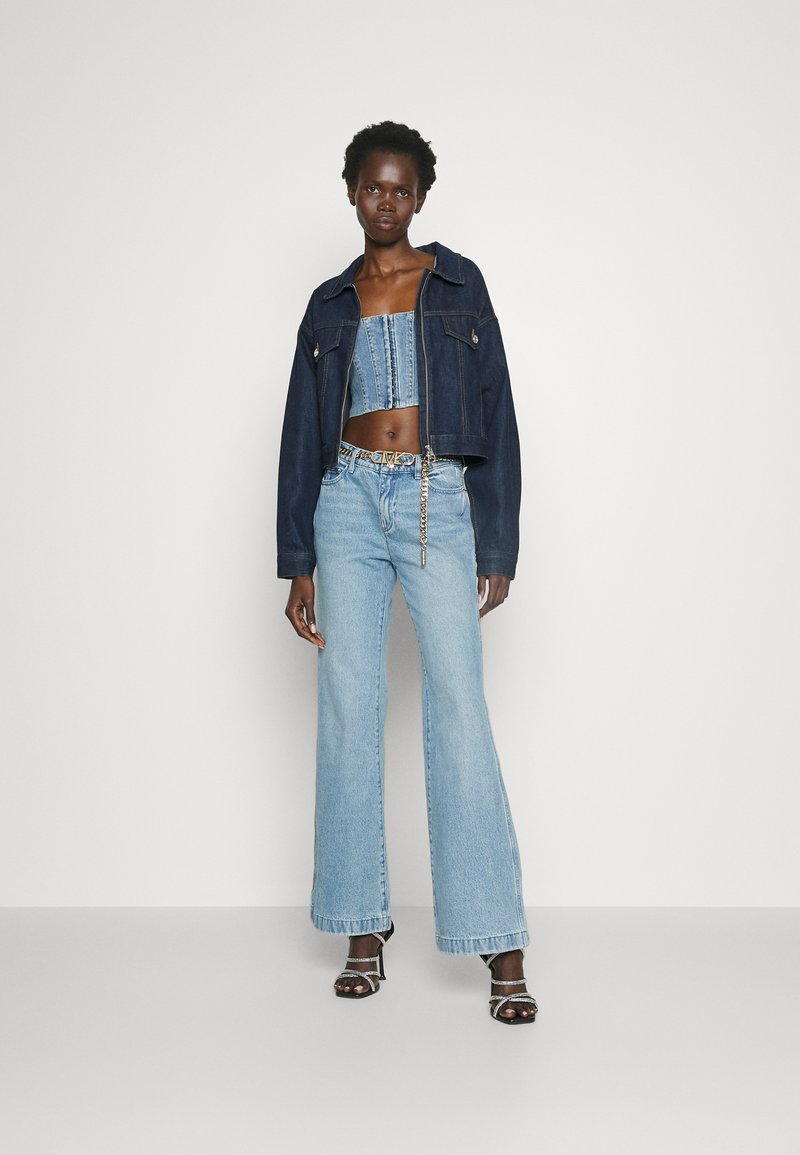 Jeansowa kurtka z krótkim krojem w ciemnoniebieskim kolorze. Pasujące jasnoniebieskie rurki z szerokimi nogawkami. Uzupełniona czarnymi sandałami na obcasie i paskiem z łańcuchem.