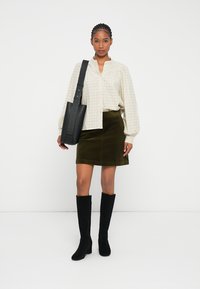 Bolso negro de hombro, blusa a cuadros color crema, falda de pana color verde oliva y botas altas negras. Texturas de tela suaves con diseño estructurado.