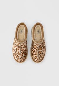 Paire de chaussons marron à imprimé léopard avec coutures blanches et doublure intérieure en peluche beige, étiquette de la marque visible à l'intérieur de chaque chausson.