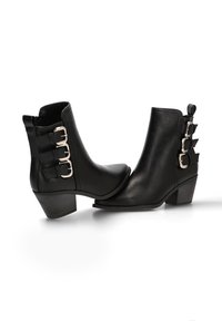 Botines de cuero negro hasta el tobillo con puntera puntiaguda, tacón bajo y cuadrado, y hebillas ajustables en el lateral. Textura suave y diseño elegante.