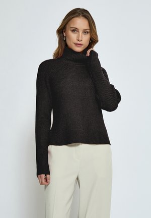 Black ribbed turtleneck sweater with long sleeves, featuring a relaxed fit and soft texture. Model pairs with light-colored trousers.