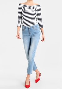 Biała i granatowa bluzka typu off-the-shoulder w paski, z rękawami do trzech czwartych, w połączeniu z jasnoniebieskimi skinny jeansami i czerwonymi szpilkami.