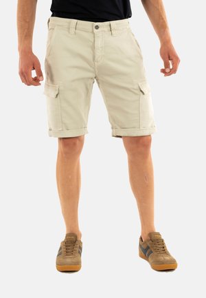 Pantalones cortos cargo color caqui con dobladillos enrollados, bolsillos delanteros y laterales, hechos de tela de algodón, combinados con zapatillas marrones con rayas azules.