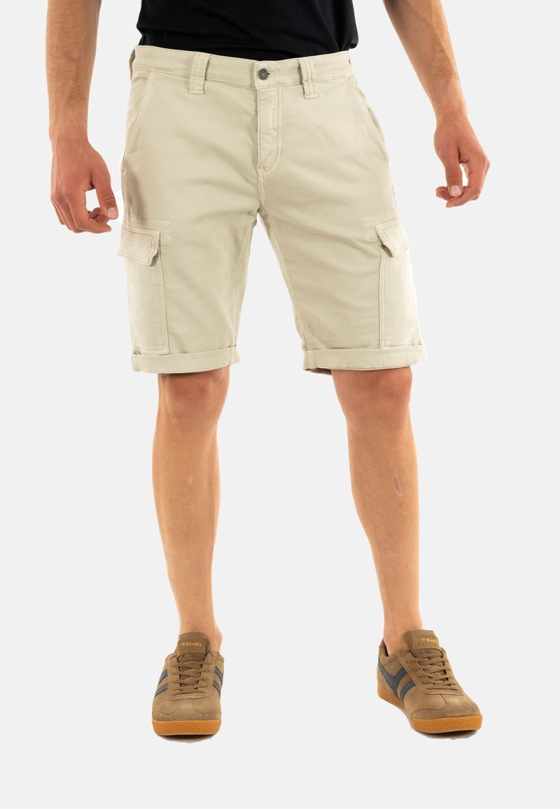 Pantaloni cargo khaki con orli arrotolati, tasche frontali e laterali, realizzati in tessuto di cotone, abbinati a sneaker marroni con strisce blu.
