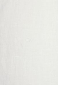 Witte linnenstof met een gestructureerde weving, met subtiele variaties. Bevat een discreet geborduurd 'CK'-logo in lichte draad.