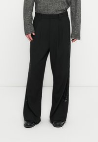 Μαύρο παντελόνι φαρδιάς γραμμής με πιέτες, διαθέτει διάφανα πλαϊνά πάνελ. Κατασκευασμένο από λείο ύφασμα, έχει μινιμαλιστικό σχεδιασμό και άνετη εφαρμογή.