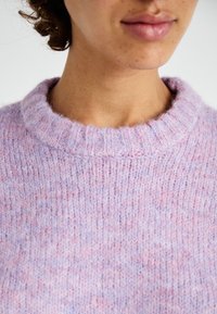 Svijetloplavi pletivi pulover s rebrastim okruglim izrezom. Ima mekan, teksturiran površinu s suptilnim ružičastim i plavim mrljama.