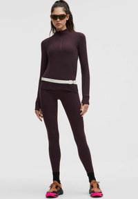 Tumši sarkans sporta garām piedurknēm krekls ar pusi rāvējslēdzēju un baltu jostu. Pieguļoši legingi, pabeigti ar melniem un rozā skriešanas apaviem.