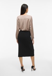 Silkefarget beige bluse med lange ermer og bakfold, parret med et tettsittende svart blyantskjørt. Svart høye hæler fullfører antrekket.