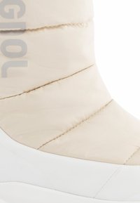 Beige gewatteerde laars met een textuur van nylon bovenwerk en een witte rubberen zool. Bevat gestikte delen en grote letters langs de zijkant.