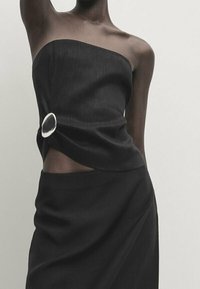 Black strapless dress featuring a twisted design with a silver ring accent at the waist. Smooth fabric with a sleek, fitted silhouette.