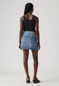 Džínová mini sukně s světlým odstínem, vysokým pasem a zadními kapsami. Obsahuje hnědou koženou nášivku s logem značky. Kombinována s černým tílkem.