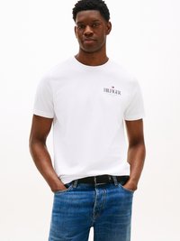 White short-sleeve T-shirt with small black "HILFIGER" logo on the chest, paired with blue jeans and a black textured belt.