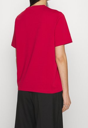 Camiseta de algodón roja con mangas cortas y cuello redondo, con un diseño simple y sin adornos. Combina con pantalones negros holgados.
