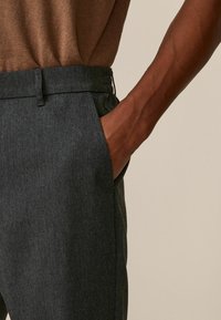 Pantalon taillé gris foncé avec une texture lisse, doté d'une poche latérale et d'une taille élastique, porté avec un haut marron.