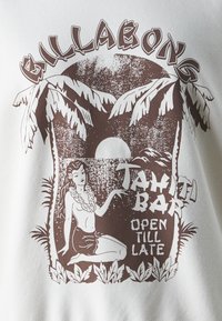 T-shirt bianco con stampa grafica marrone che raffigura una donna con una collana di fiori, circondata da palme e il testo "Tahiti Bar Aperto Fino a Tardi."