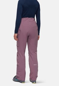 Ski pants in soft mauve fabric with adjustable waist, cargo pocket on left thigh, and reinforced lower legs. Smooth texture with subtle branding.