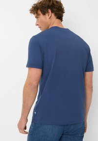 T-shirt in cotone blu navy con maniche corte, colletto rotondo e un piccolo etichetta decorativa sul lato inferiore. Tessuto liscio, vestibilità casual.