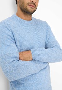 Helles blaues Strickpullover mit Rundhalsausschnitt und langen Ärmeln. Merkmale des strukturierten Stoffes mit einem subtilen, melierten Muster.